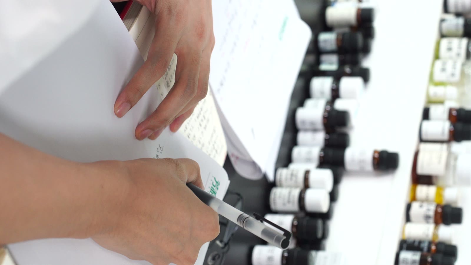 A formulator writing a blend in a notebook beside rows of sample bottles
